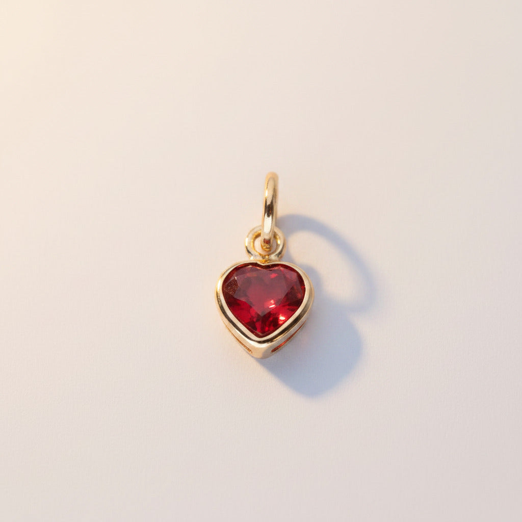 A gold heart-shaped charm with a red heart-shaped stone, shown on a light background with a repeating watermark pattern.