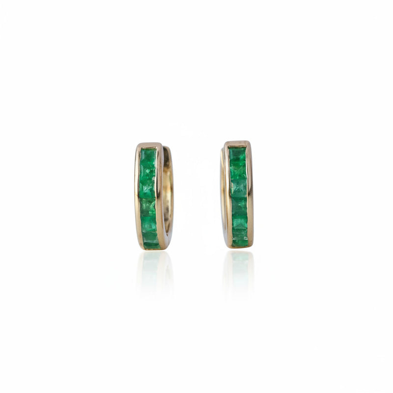 A pair of gold hoop earrings with a channel-set row of green emerald-cut stones, displayed on a light reflective surface.