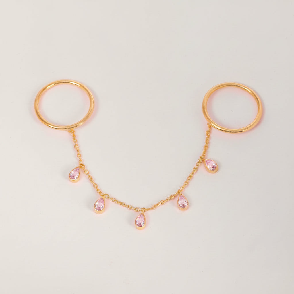 Rose gold double hoop body jewelry connected by a delicate chain with five small pink teardrop rhinestones, displayed on a light gray background.