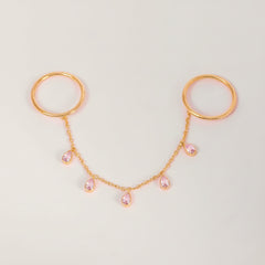 Rose gold double hoop body jewelry connected by a delicate chain with five small pink teardrop rhinestones, displayed on a light gray background.