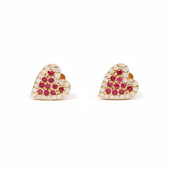A pair of gold heart-shaped stud earrings adorned with small clear crystals and red gemstones, displayed on a light pink background with a diagonal repeating watermark pattern.
