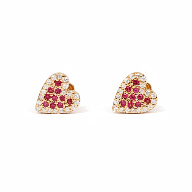 A pair of gold heart-shaped stud earrings adorned with small clear crystals and red gemstones, displayed on a light pink background with a diagonal repeating watermark pattern.