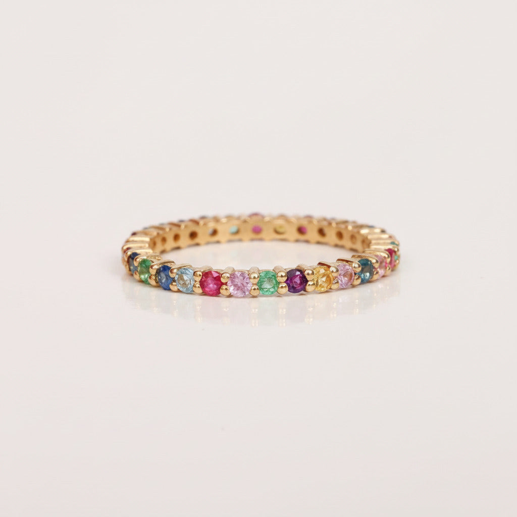 A gold-plated eternity bracelet featuring a row of round-cut multicolor gemstones, displayed on a light gray background with a repeating 'MINIMAL ATELE' watermark pattern.