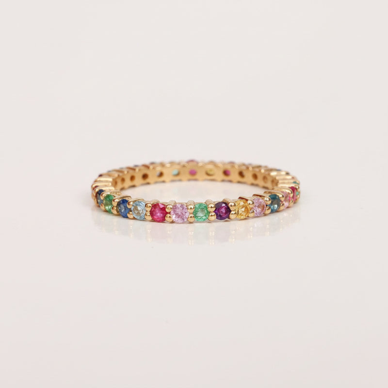A gold-plated eternity bracelet featuring a row of round-cut multicolor gemstones, displayed on a light gray background with a repeating 'MINIMAL ATELE' watermark pattern.
