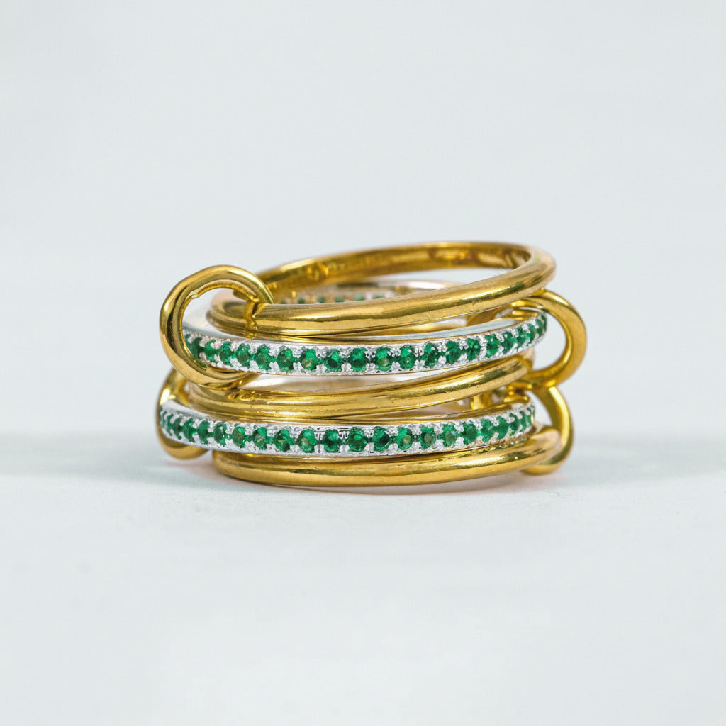 A stack of three gold bangles, with two featuring a row of small green stones, photographed on a light gray background with a faint watermark.