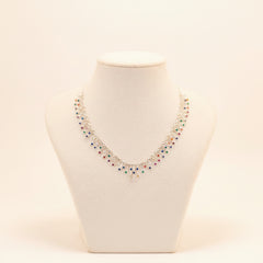 A silver-toned statement necklace with multiple dangling colorful gemstone clusters, displayed on a white fabric mannequin bust against a gray background.