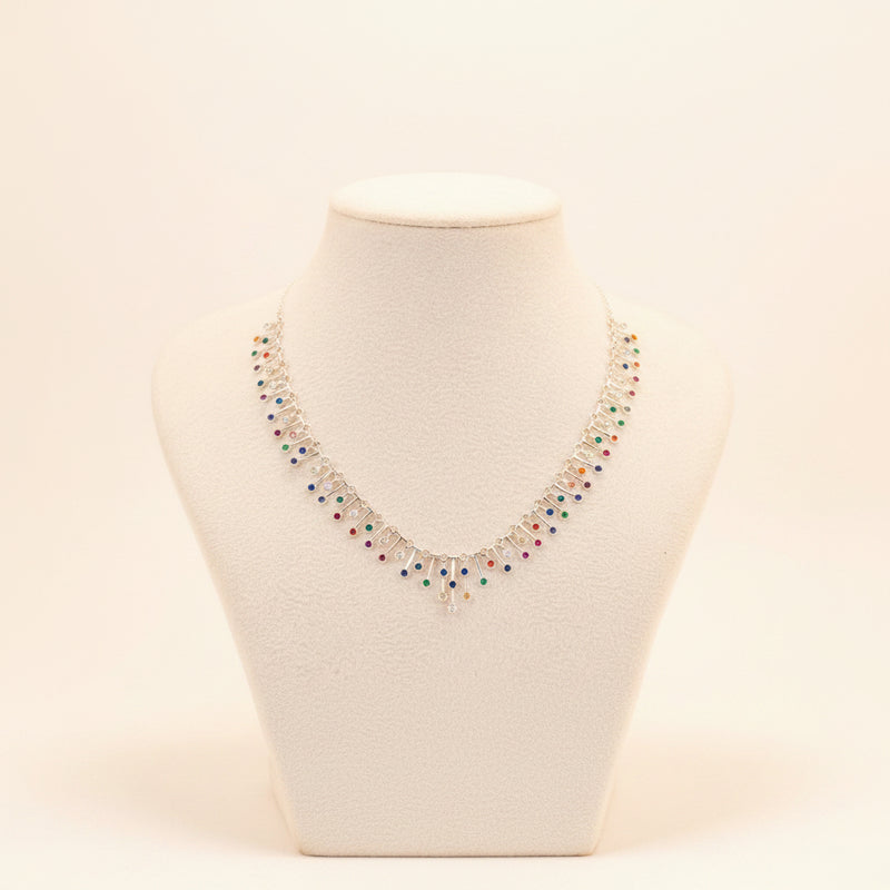A silver-toned statement necklace with multiple dangling colorful gemstone clusters, displayed on a white fabric mannequin bust against a gray background.