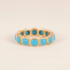 A gold-plated eternity-style ring featuring a row of round turquoise cabochon stones, displayed on a light gray background with a repeating watermark.