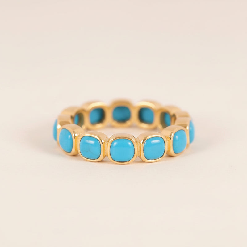 A gold-plated eternity-style ring featuring a row of round turquoise cabochon stones, displayed on a light gray background with a repeating watermark.
