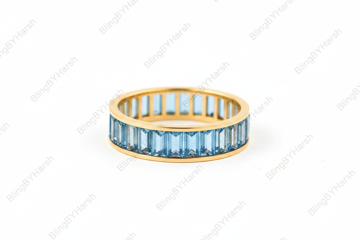 A gold ring with a row of blue baguette-cut gemstones, displayed on an antique book with a lace cloth nearby.