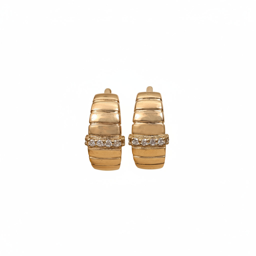 A pair of gold hoop earrings with a textured, ribbed design and a row of clear stones across the front, displayed on a two-toned beige and white background.