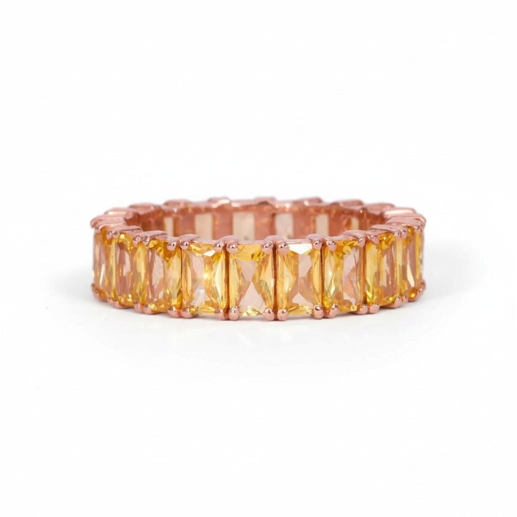 A rose gold eternity band featuring a row of rectangular yellow-orange cushion-cut crystals, shown on a white background with a faint diagonal watermark pattern.