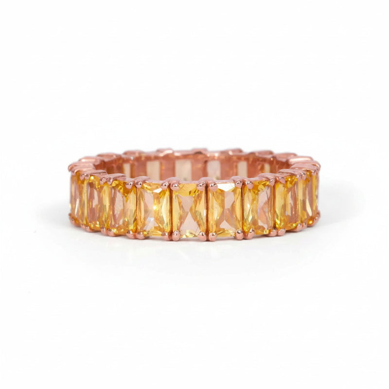 A rose gold eternity band featuring a row of rectangular yellow-orange cushion-cut crystals, shown on a white background with a faint diagonal watermark pattern.