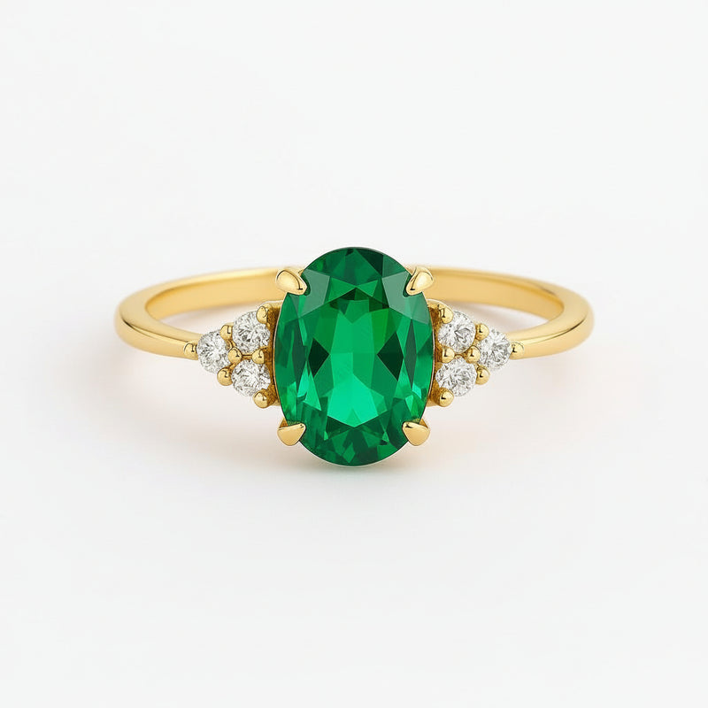 A yellow gold ring featuring a large oval-cut green emerald gemstone in the center, accented by small clear stones on either side of the band, set against a clean white background.