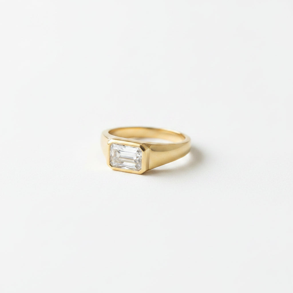 A gold ring with a rectangular clear gemstone resting on an old book with lace draped over it.