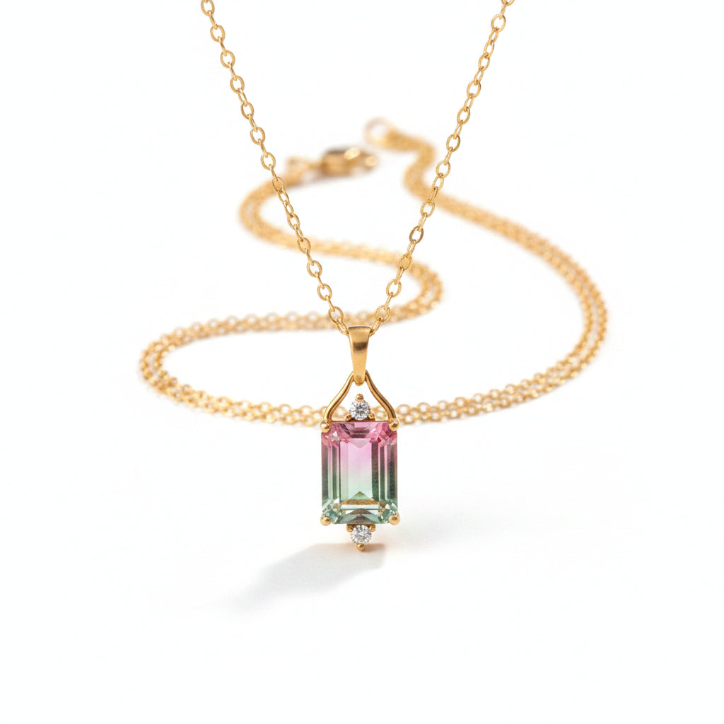 A gold pendant necklace featuring an emerald-cut multicolor gemstone with pink, green, and blue iridescence, accented by small clear stones, displayed on a beige satin fabric background.