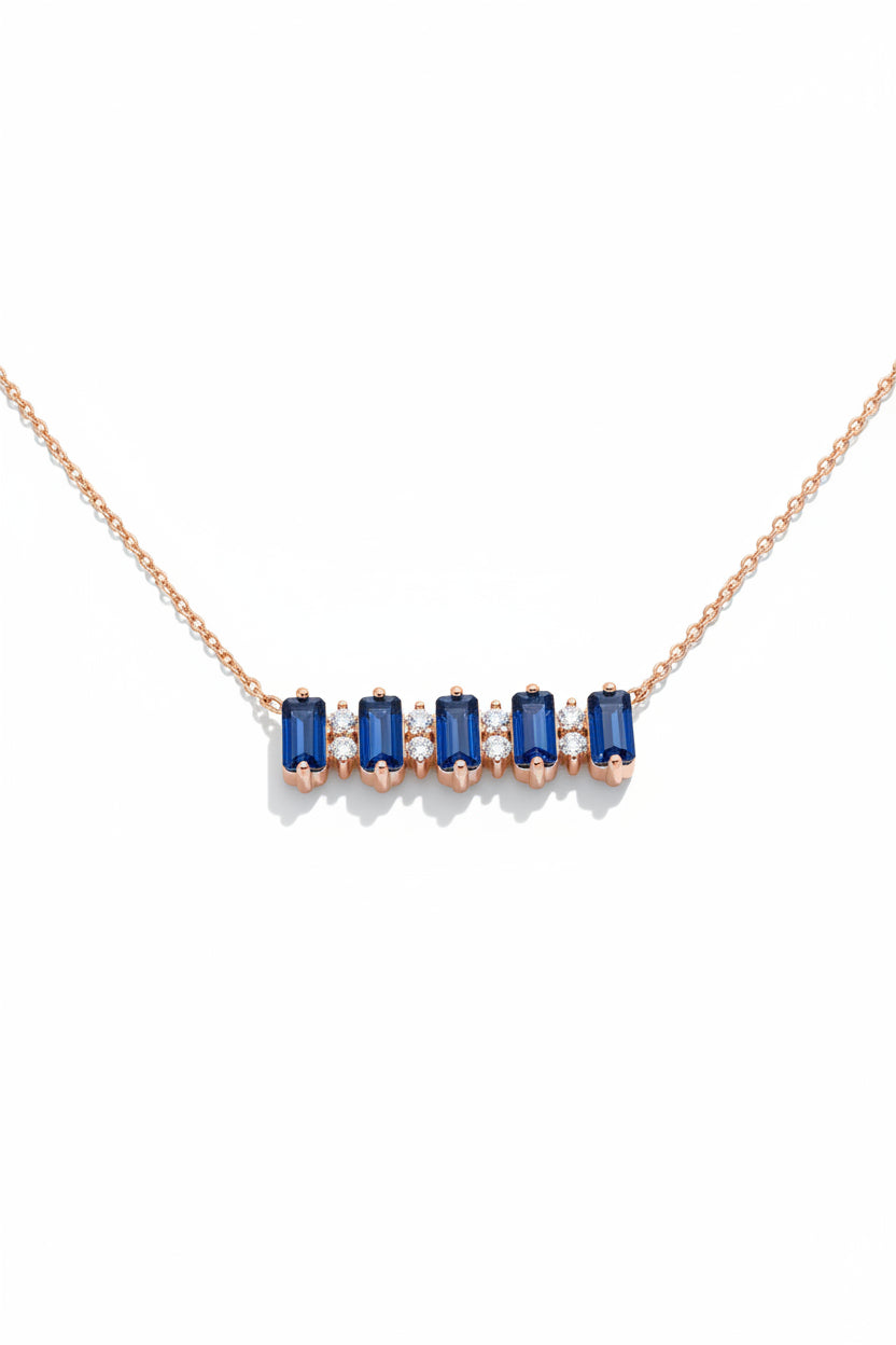 A rose gold necklace with five rectangular blue gemstones and small clear accent stones, displayed on a beige satin-lined jewelry box.