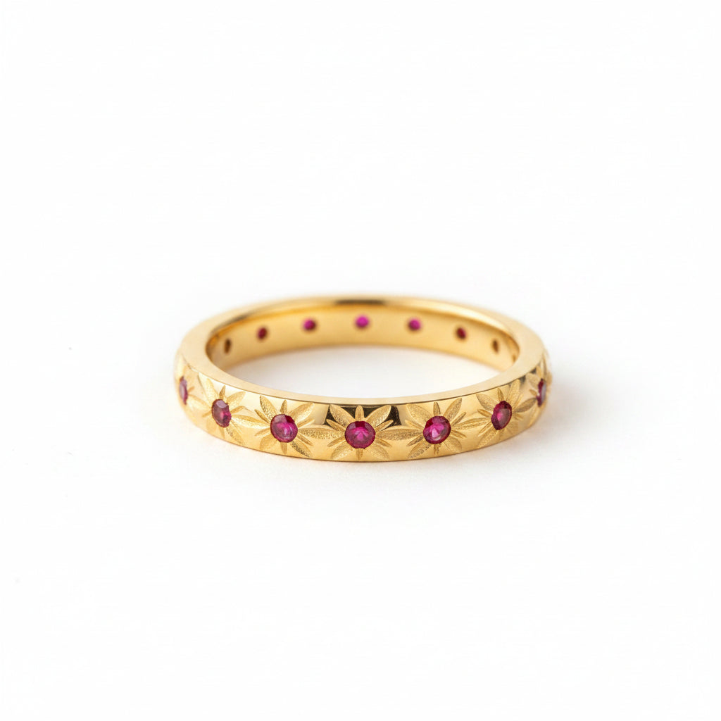 A gold eternity ring with small red gemstones and floral star motifs, resting on a textured cream lace surface with dried flower petals.