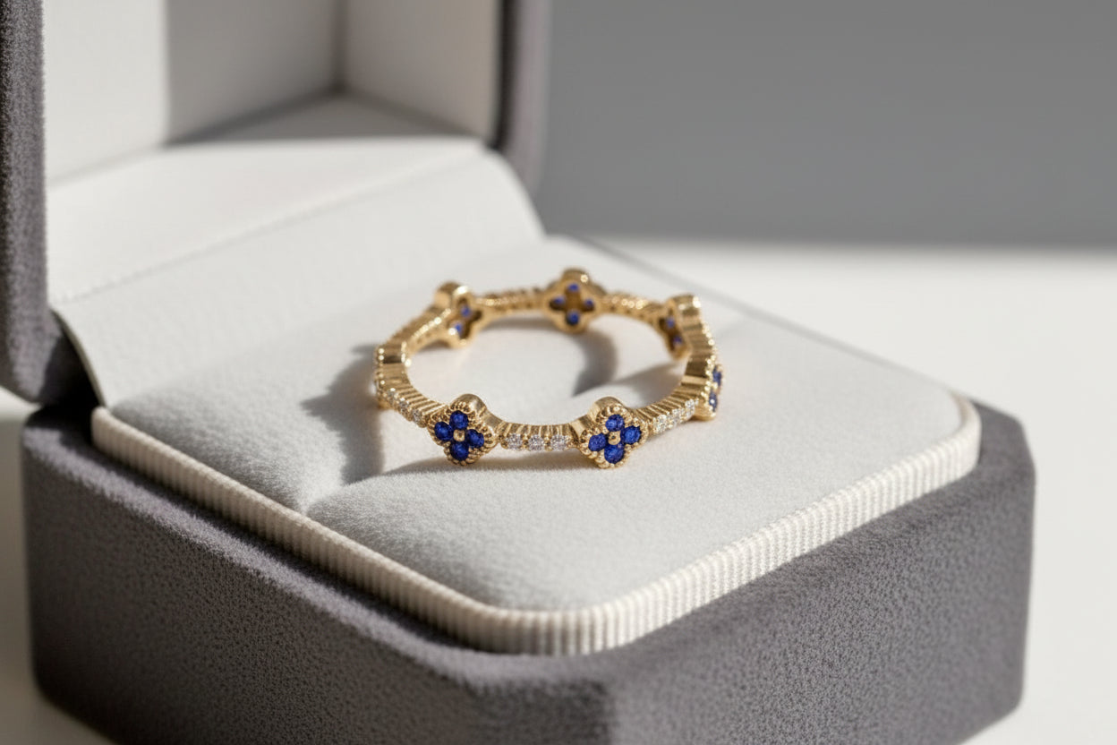 A gold chain bracelet with blue and white floral motifs, displayed inside an open gray jewelry box on a white cushion.