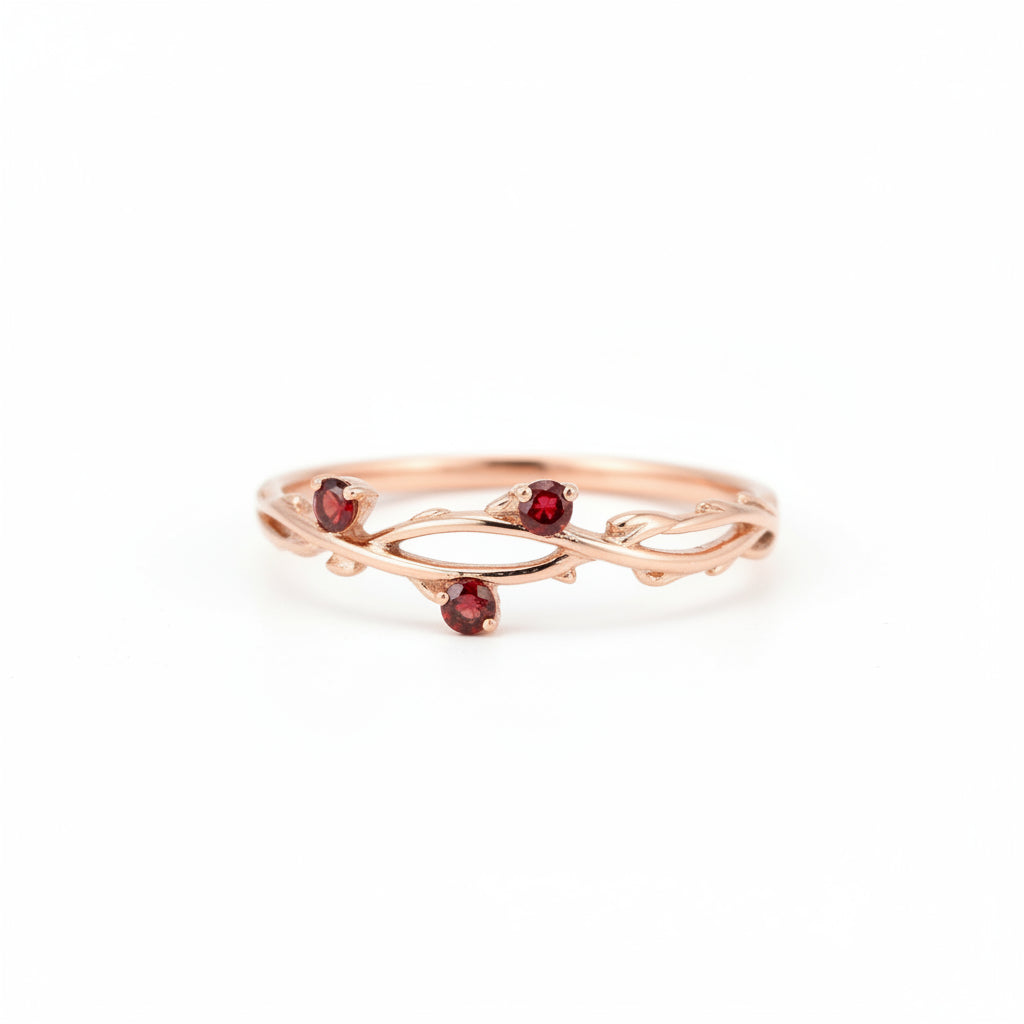 A delicate rose gold ring with three small red gemstone accents, resting on a textured stone surface with a blurred natural background.