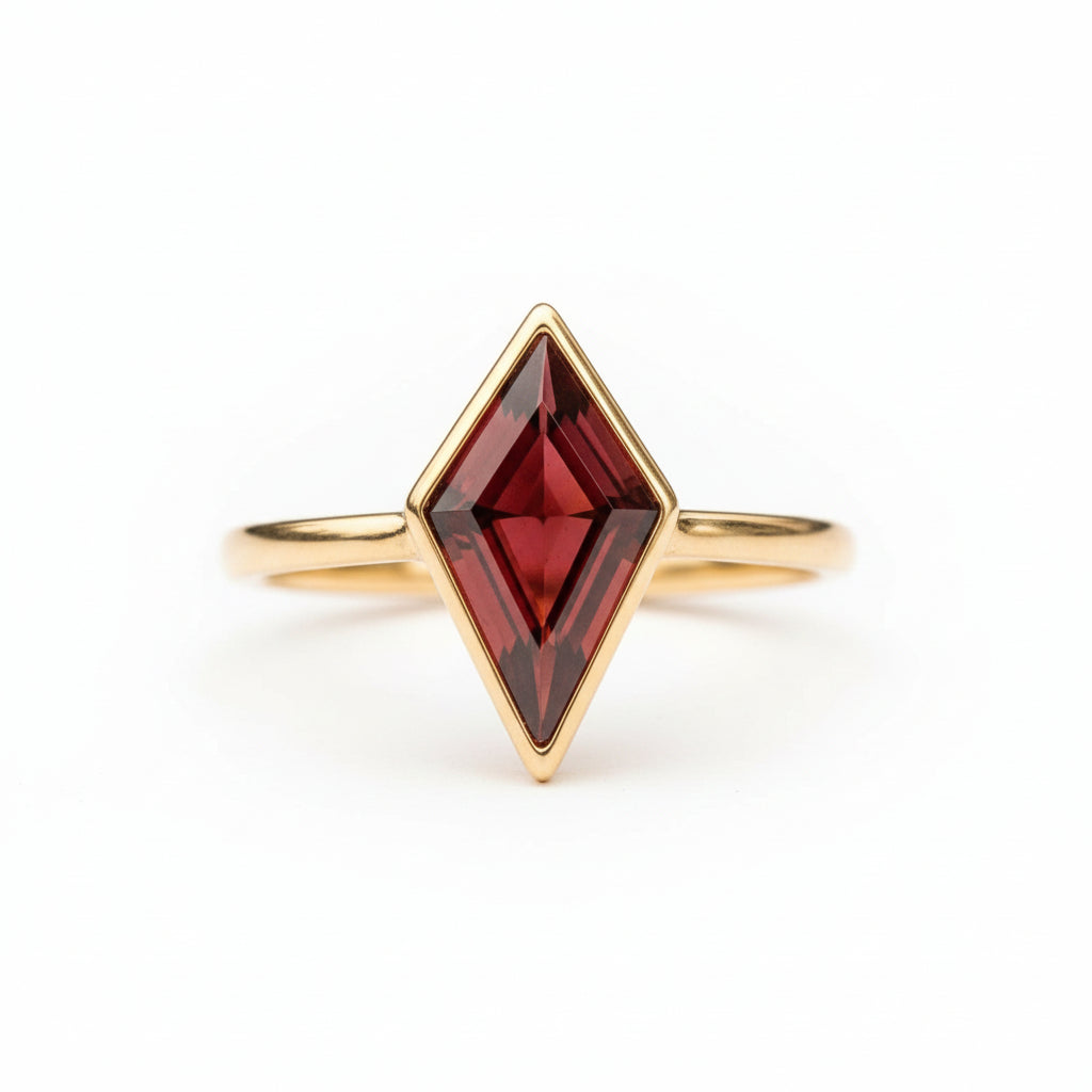 A gold ring with a large, faceted red gemstone in a diamond shape, resting on a textured stone surface with a blurred natural background.