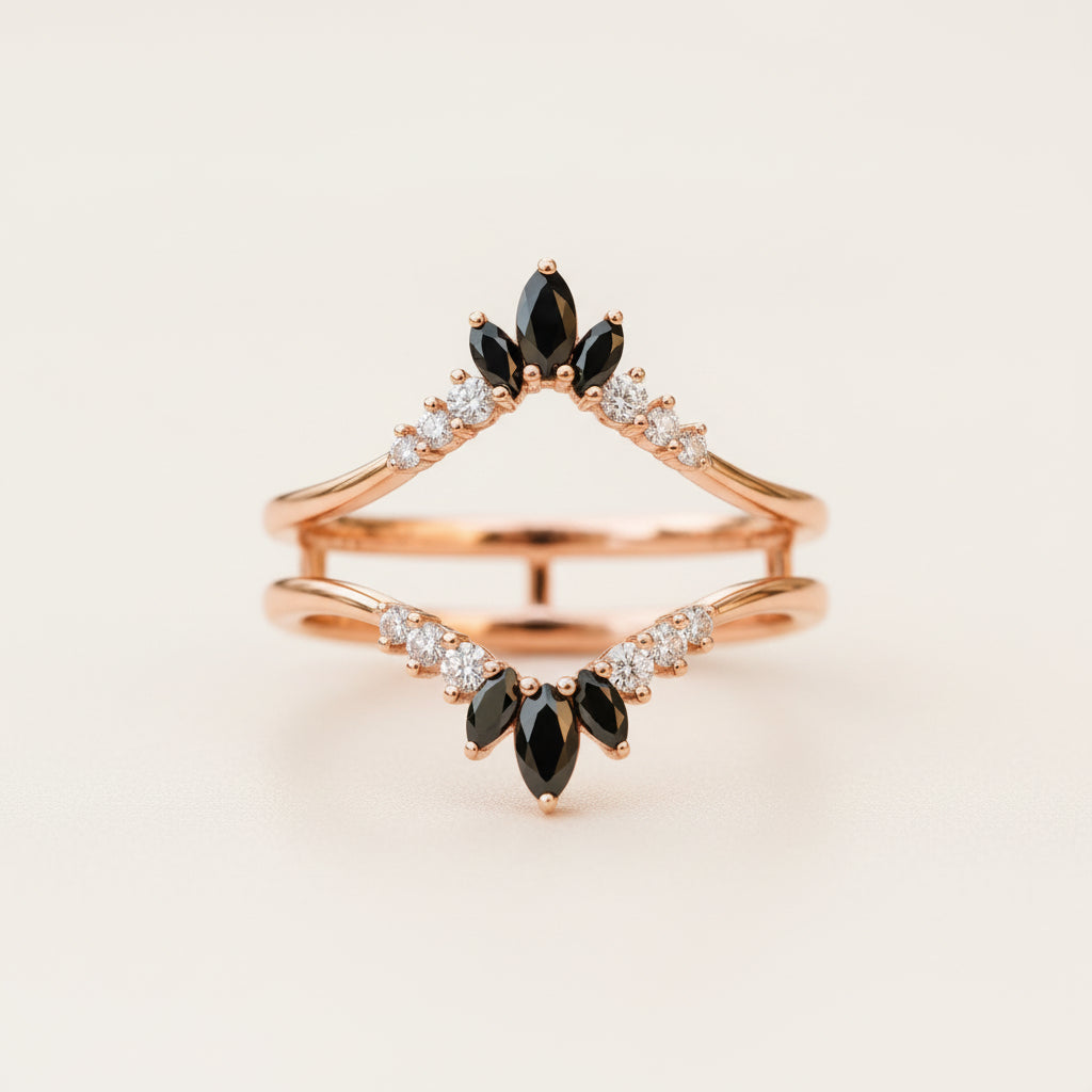 A rose gold double ring set with marquise-cut black gemstones and small clear accent stones, displayed on a textured stone surface with a blurred natural background.
