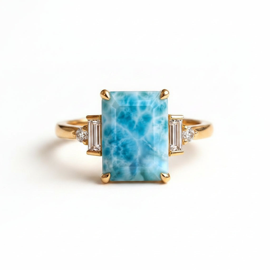 A gold ring with a large rectangular blue marbled stone and small side stones, displayed on an old brown book with lace in the foreground.