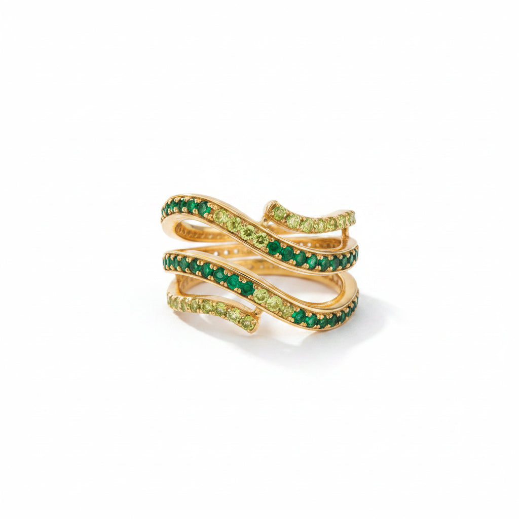 A gold ring with a snake-like coiled design, embellished with rows of green emerald-cut stones and small yellow stones, displayed on a textured gray surface.