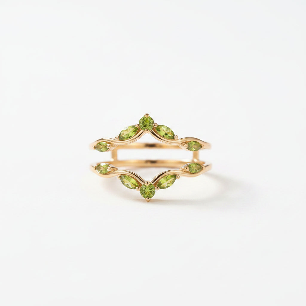 A gold ring with green gemstones displayed inside an open vintage-style jewelry box with a green velvet cushion and a cream satin interior printed with a crest and 'EST. 1920'.