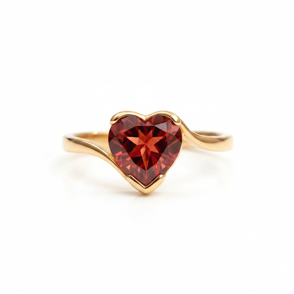 Gold ring with a heart-shaped red gemstone on a textured surface with green leaves in the background