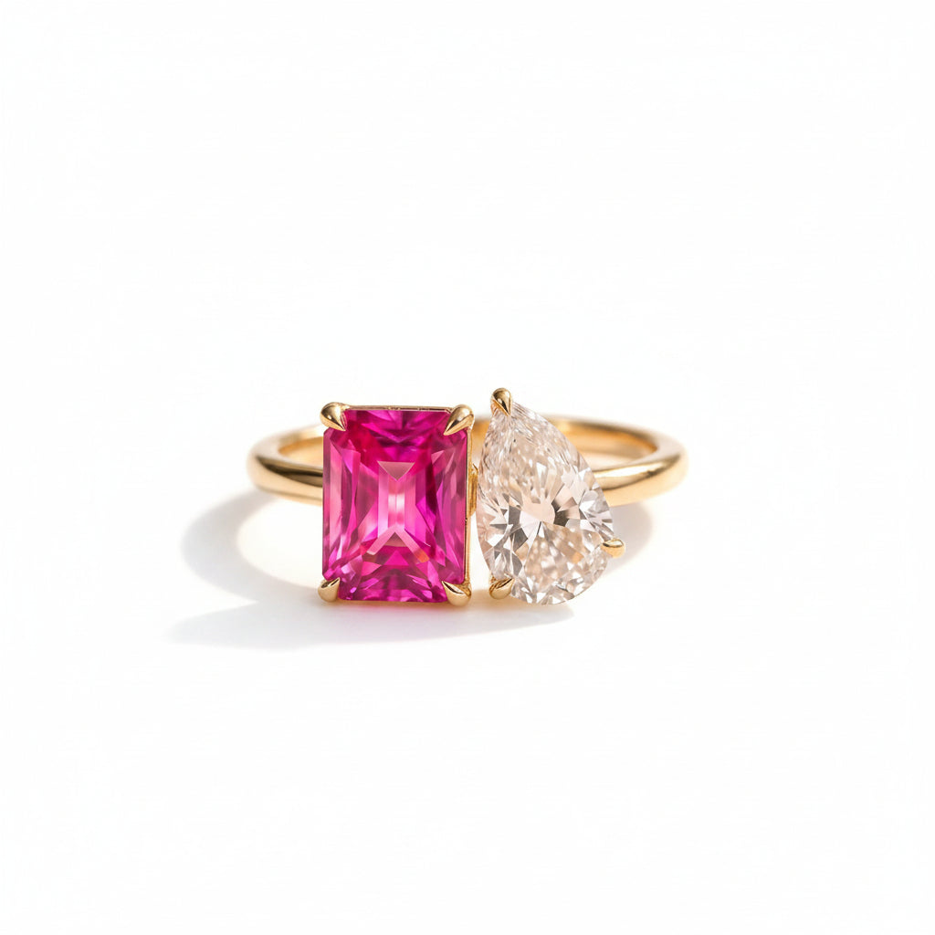 Gold ring with a pink gemstone and diamond on a textured surface with green leaves in the background