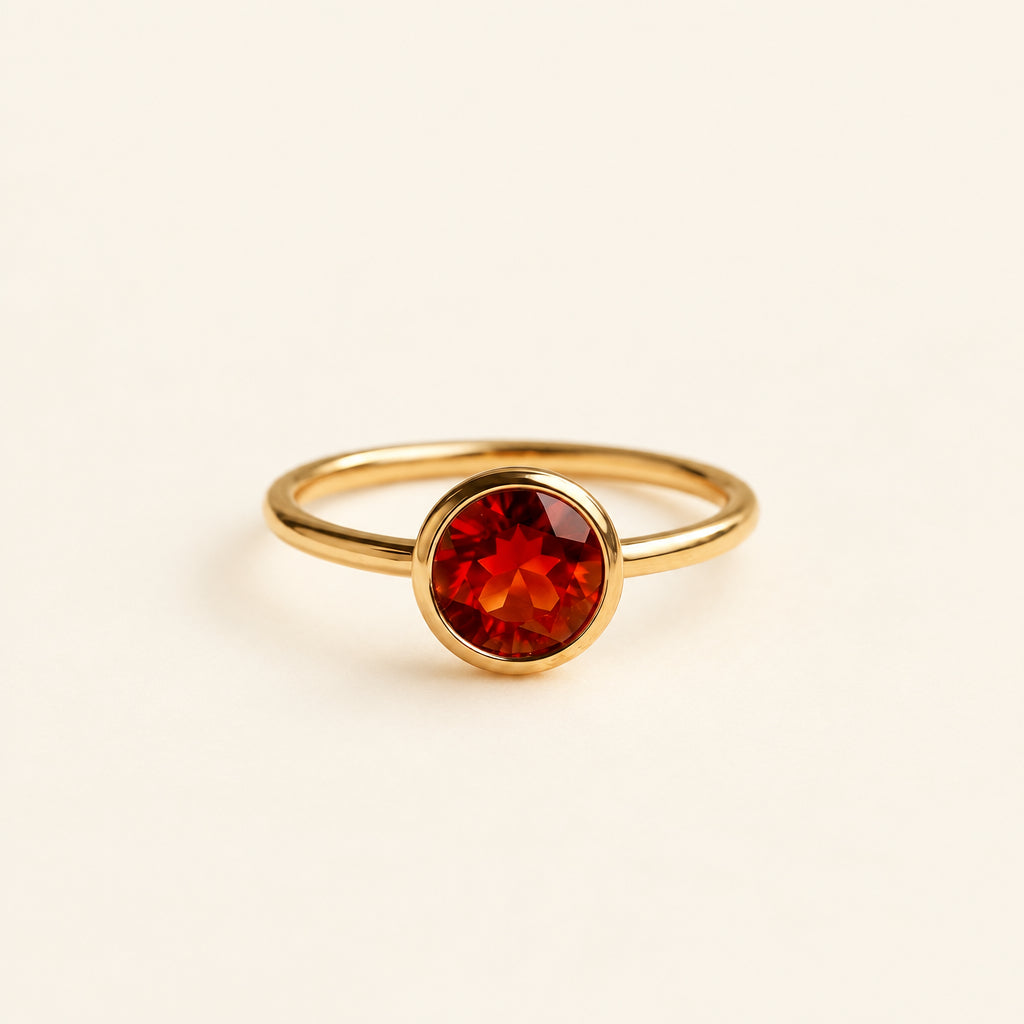 Gold ring with a red gemstone on a textured surface with green leaves in the background