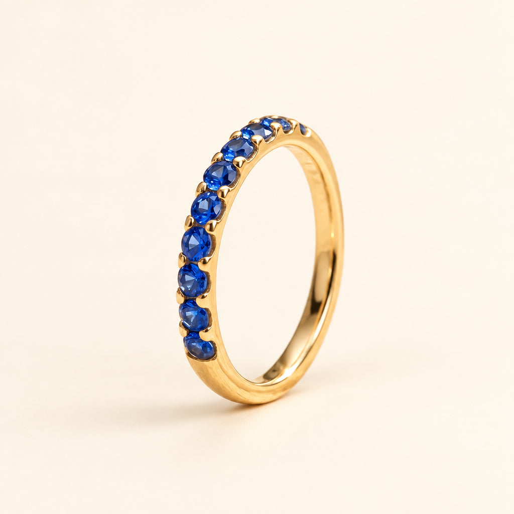 Gold ring with blue gemstones on a textured surface with blurred green leaves in the background