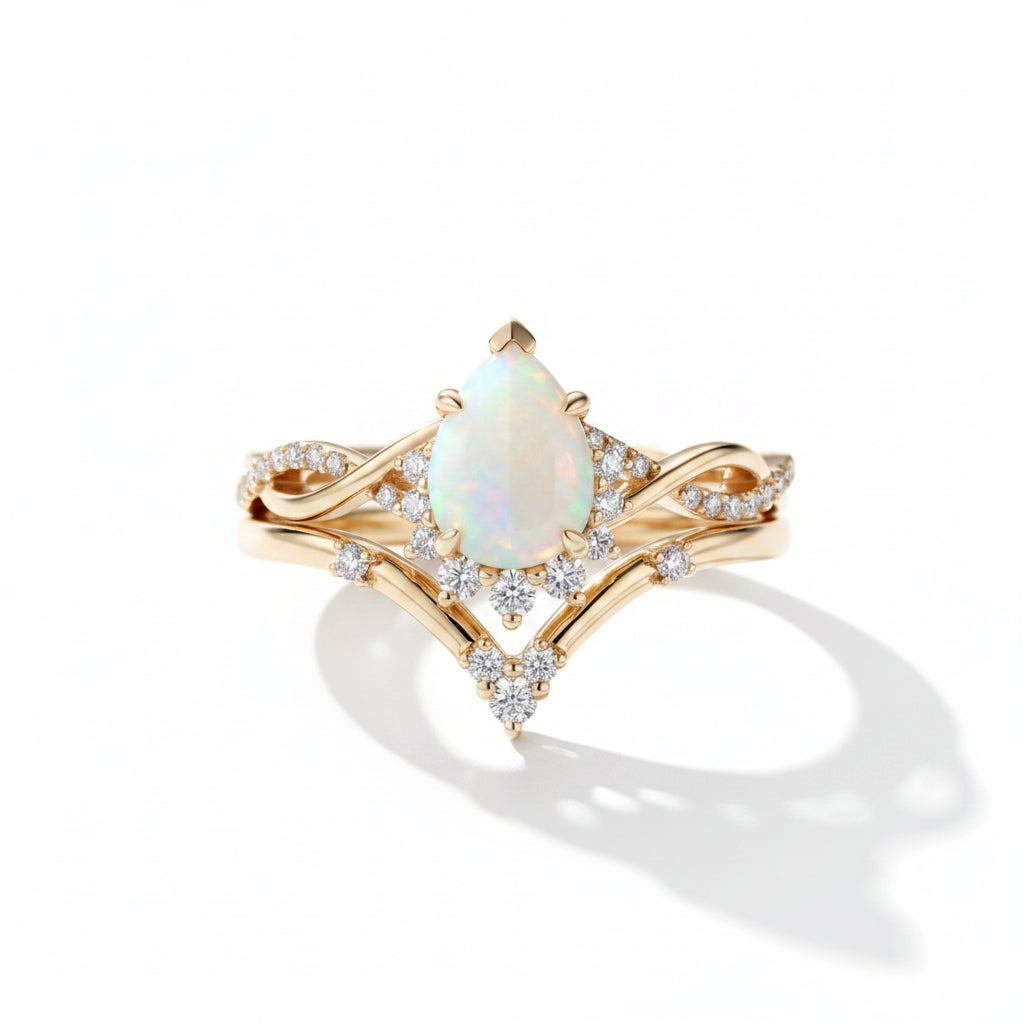 A gold ring with a pear-shaped iridescent opal center stone and small clear accent stones, photographed on a dark gray surface with a gray box in the background.