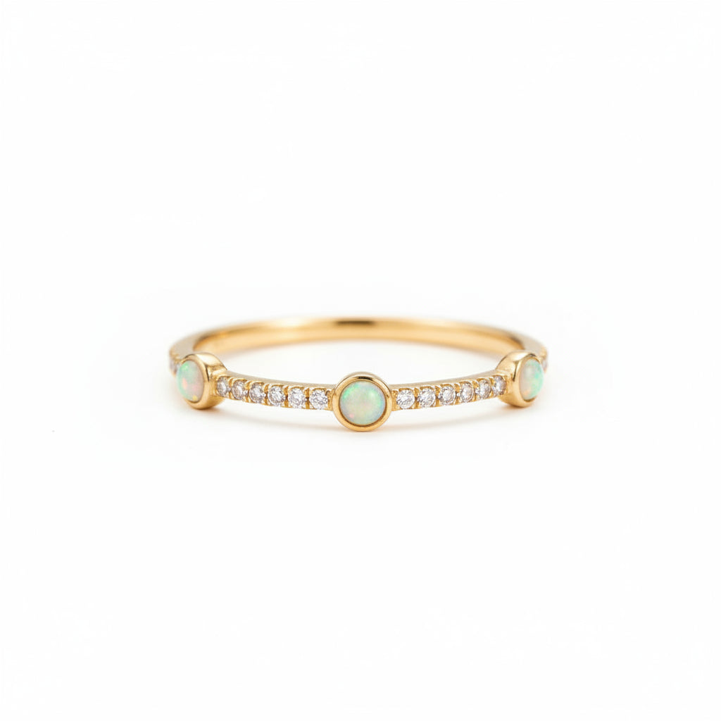 A gold bangle bracelet with three round opal gemstones and a row of small clear stones in the center, displayed on an old brown book with lace and warm bokeh lights in the background.