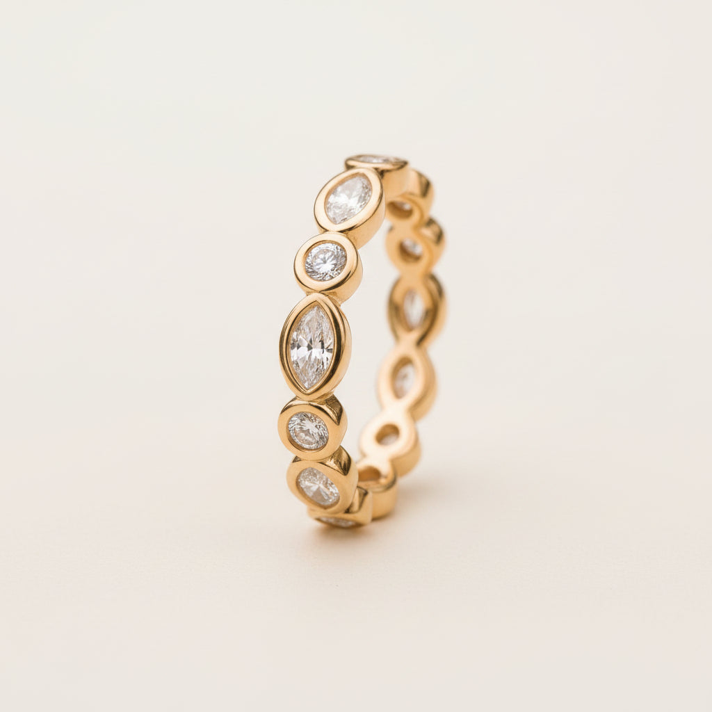 A gold eternity-style ring with marquise and round-cut clear stones, photographed resting on a textured stone surface with blurred green foliage in the background.