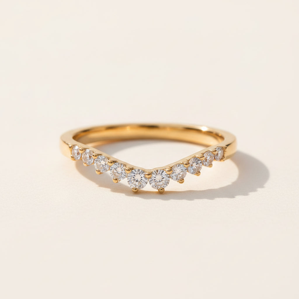 A gold band ring with a wavy, diamond-encrusted front, resting on a textured stone surface with a blurred natural background.