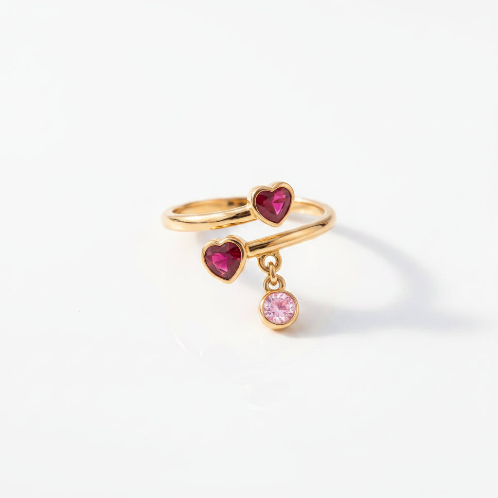 Gold heart-shaped ring with red and pink gemstones on a textured surface with flowers.