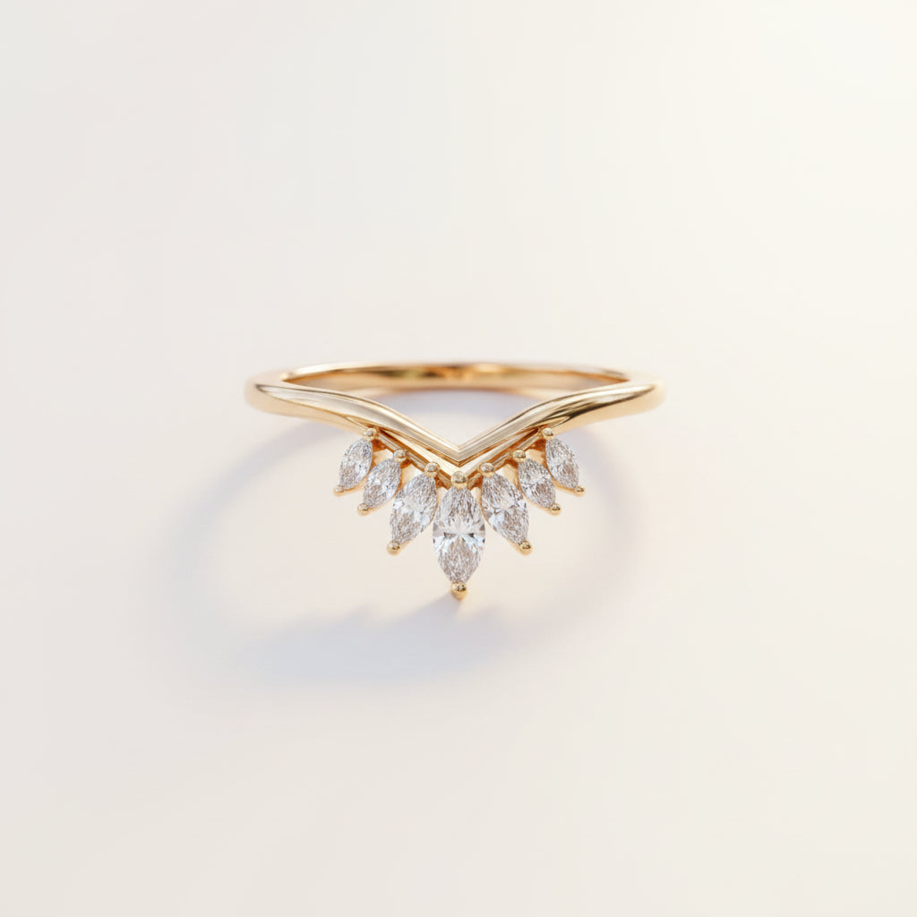 A gold ring with a V-shaped band and a cluster of marquise-cut clear stones, resting on a textured stone surface with a blurred green background.