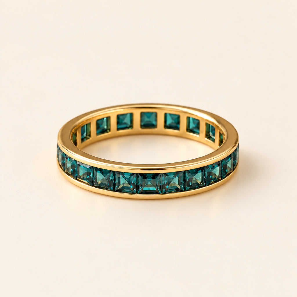 Gold ring with green gemstones on a textured surface with lavender