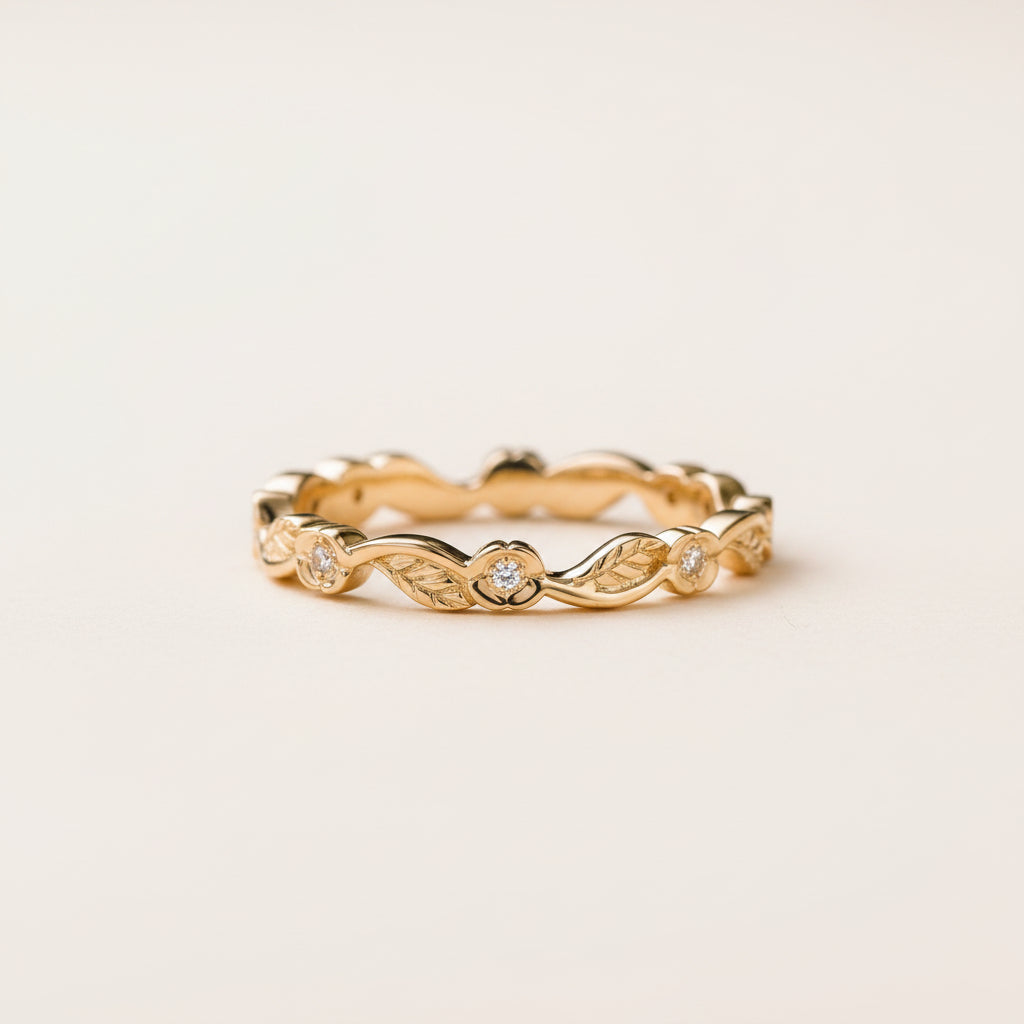 A delicate yellow gold eternity band ring with small round-cut diamonds set in a wavy, leaf-like pattern, resting on a textured stone surface with a blurred natural background.