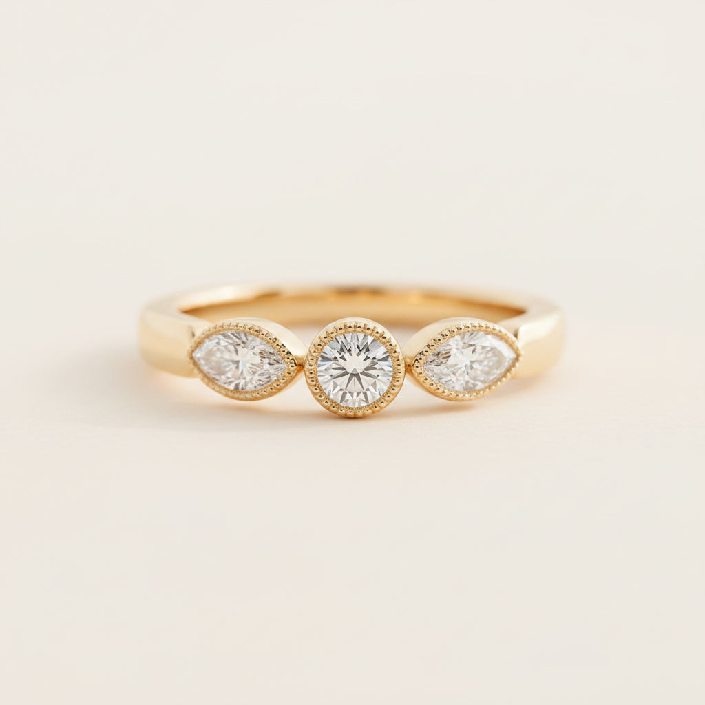 A gold three-stone ring with round-cut center stones and marquise-cut side stones, resting on a textured stone surface with a blurred green background.
