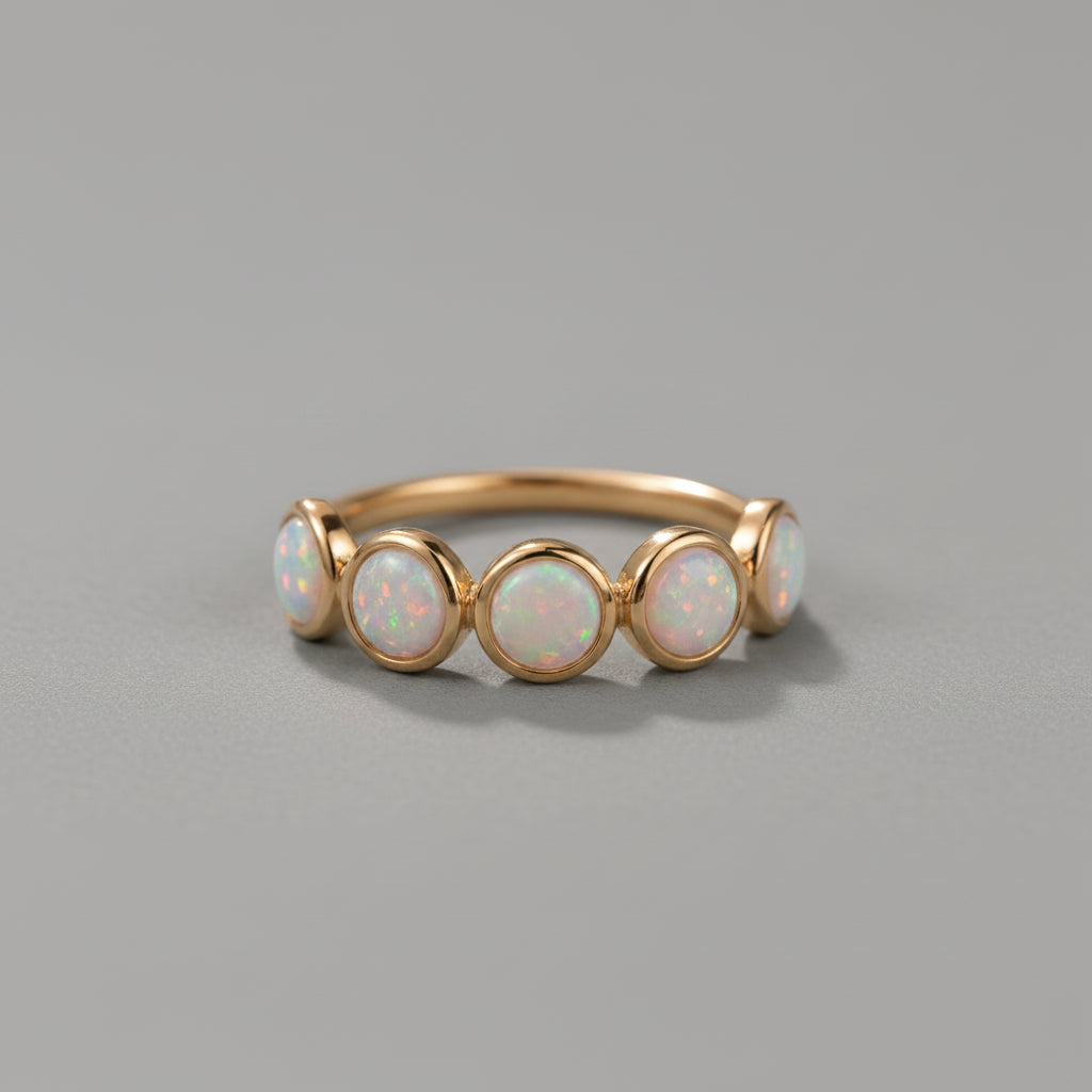 A gold ring featuring five round iridescent opal gemstones, displayed on a soft, draped white fabric background.