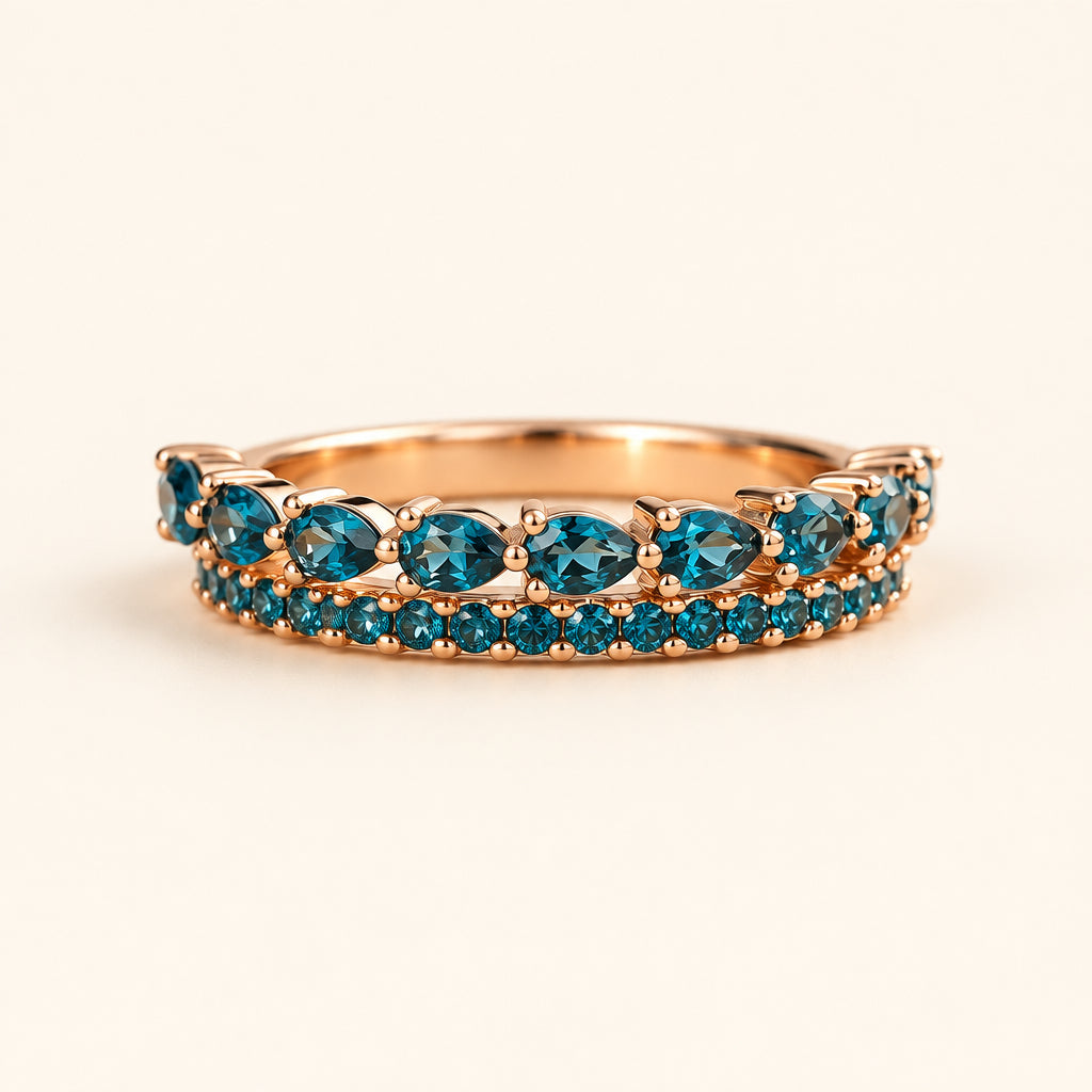 A rose gold eternity ring featuring marquise-cut and round deep blue gemstones, resting on a textured stone surface with a warm, blurred natural background.