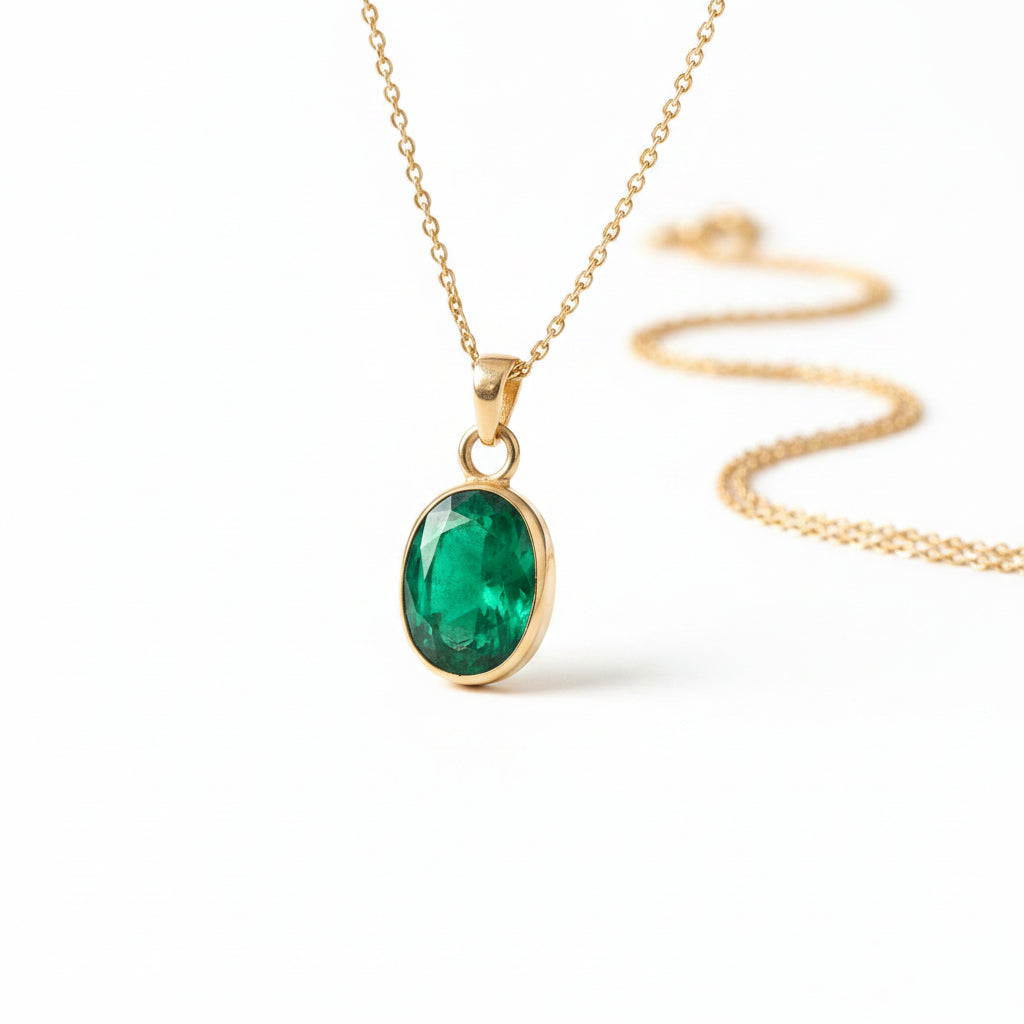 A gold pendant necklace with a faceted green emerald-cut stone, draped over vintage leather-bound books and cream lace on a wooden surface.
