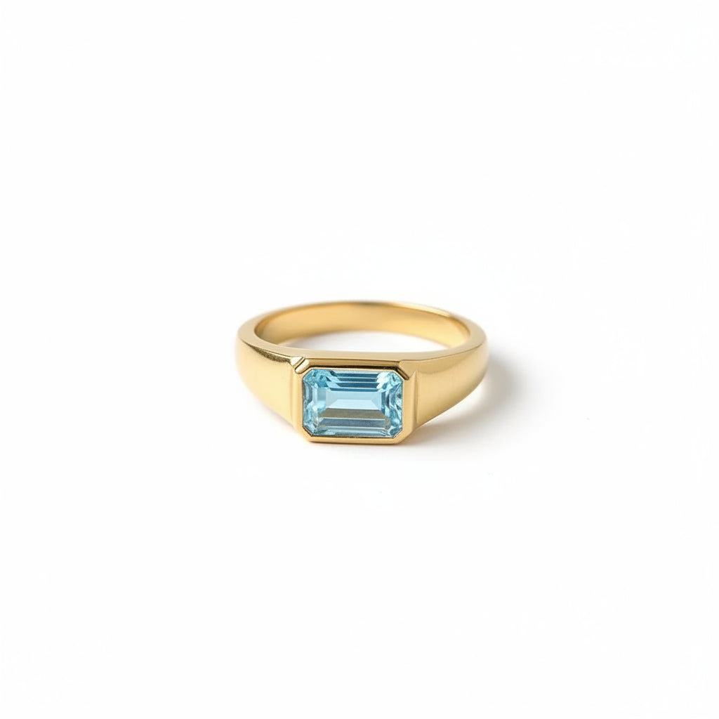 A gold ring with a rectangular light blue gemstone resting on an old book draped with beige lace.