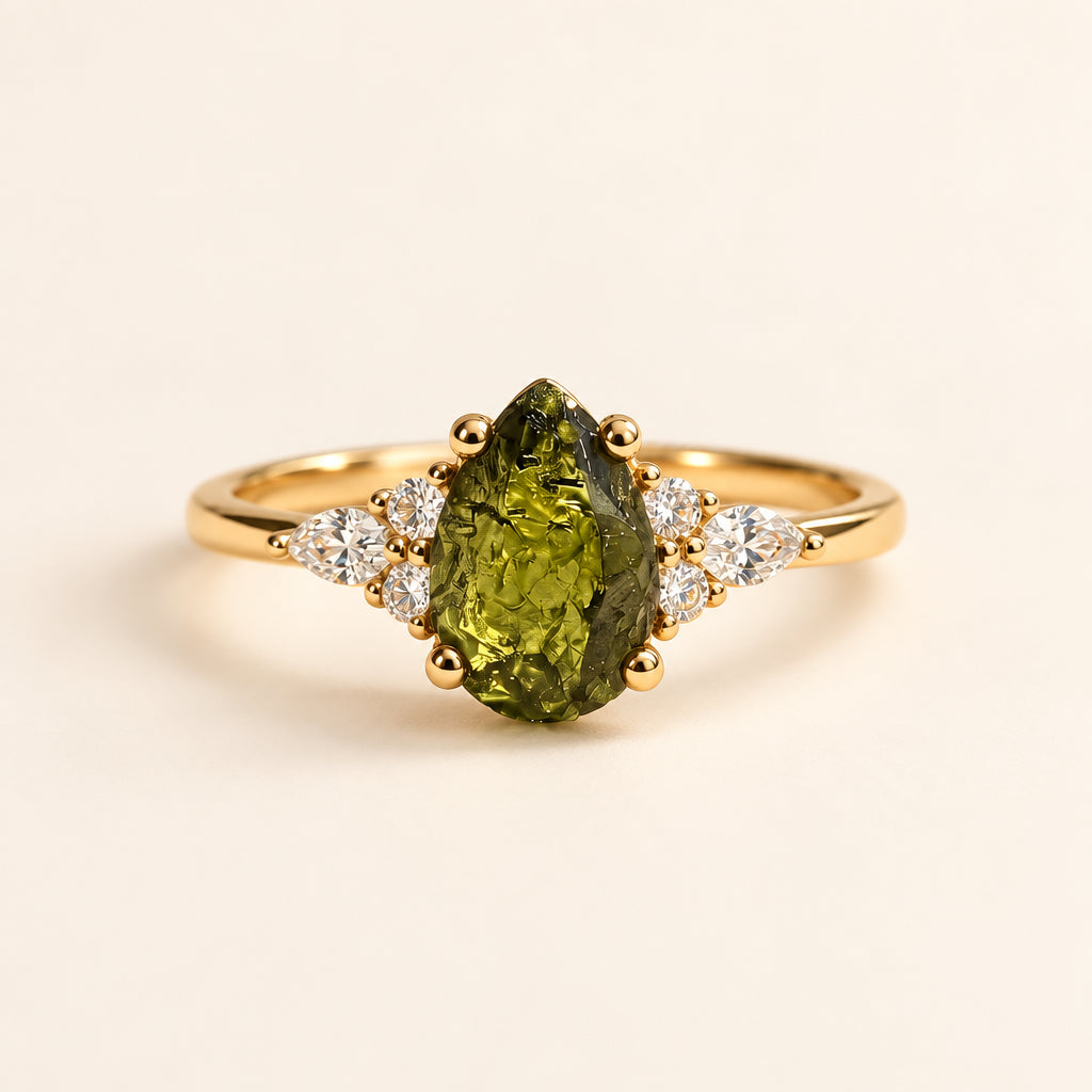 Gold ring with a green gemstone on a textured surface with leaves in the background