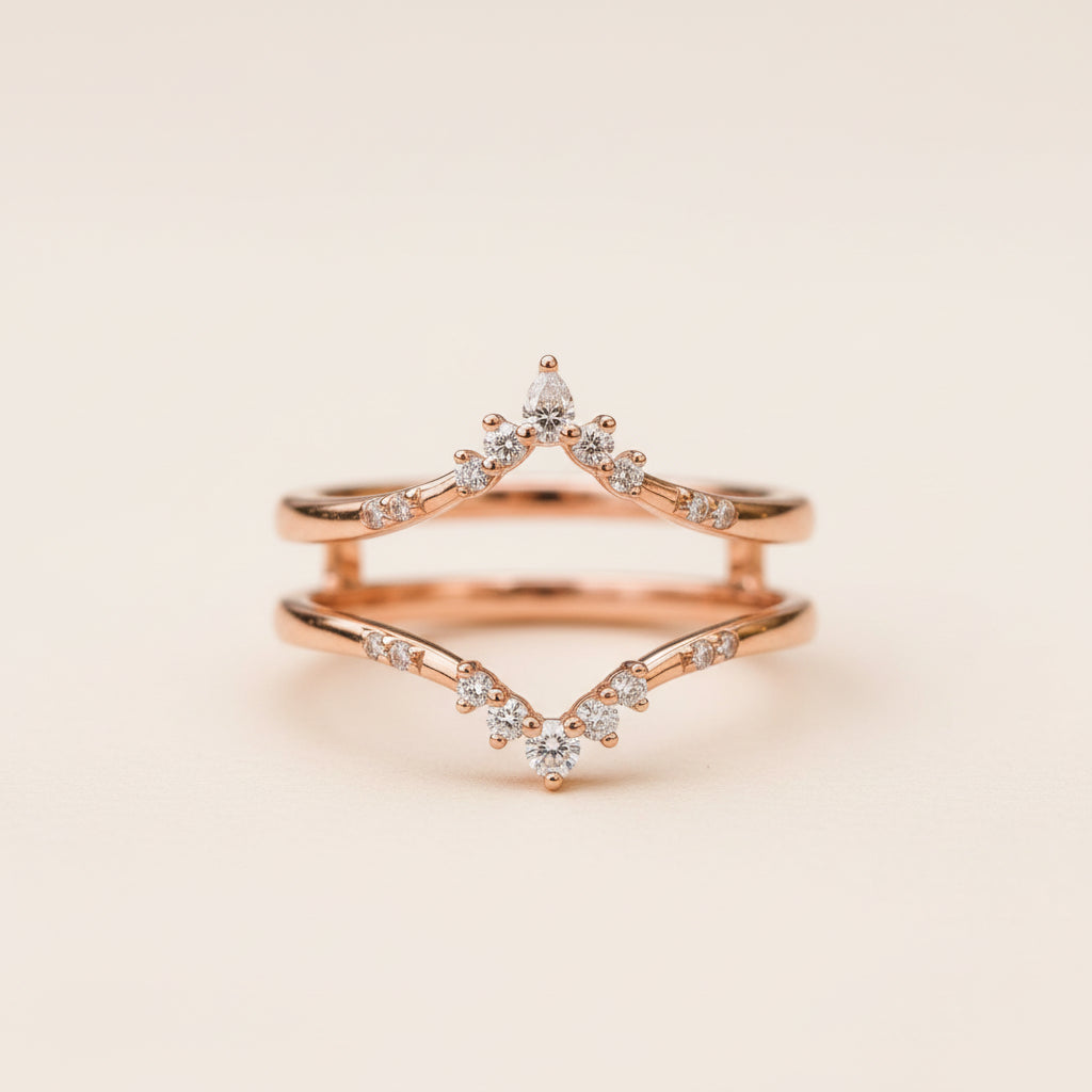 A pair of rose gold wedding rings with clear marquise and round diamonds, stacked on a textured stone surface with a blurred natural background.