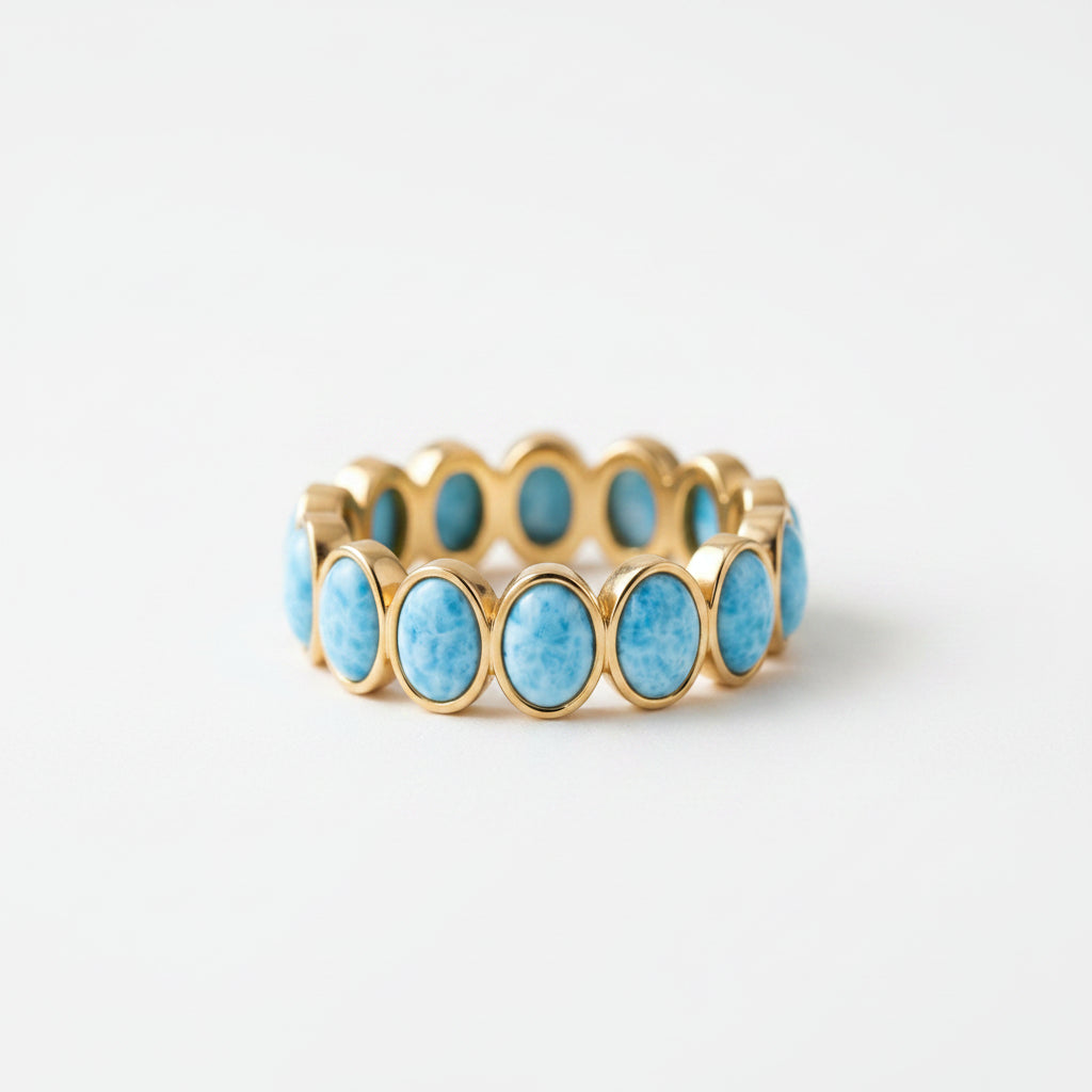 A gold-tone stretch bracelet with oval turquoise-blue marbled stones, displayed on an antique brown leather book with lace fabric beside it.