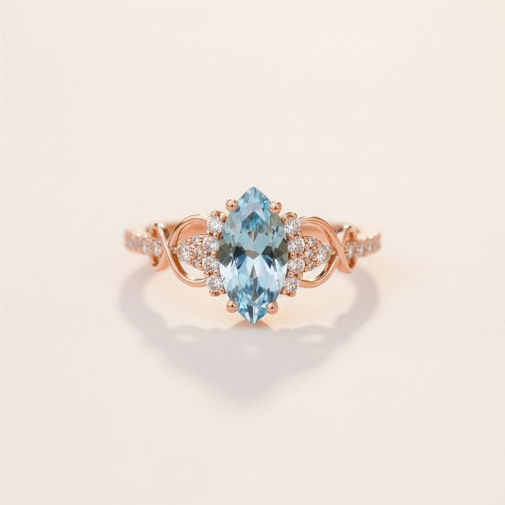 A rose gold ring with a marquise-cut light blue gemstone and small clear accent stones, resting on a textured stone surface.